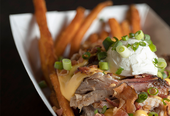 Photo of loaded sweet potato fries in a paper basket. Fries have pork, bacon, cheese, sour cream, chives.