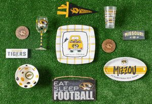 Photo of Mizzou dishware such as plates bowls and wine glasses on a green background.
