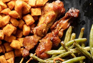 Photo of chicken satay on sticks surrounded by home fries and green beans.