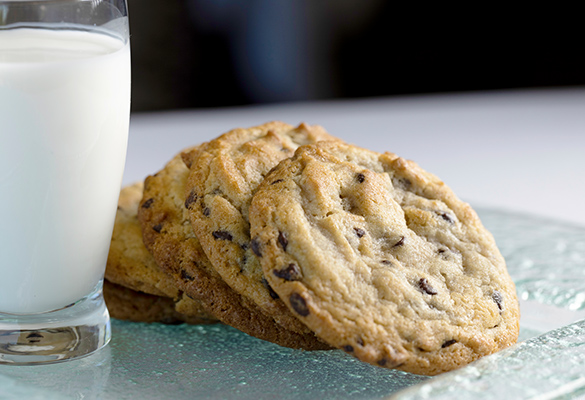 Photo of five chocolate cookies stacked on a glass plate next to a glass of white milk.