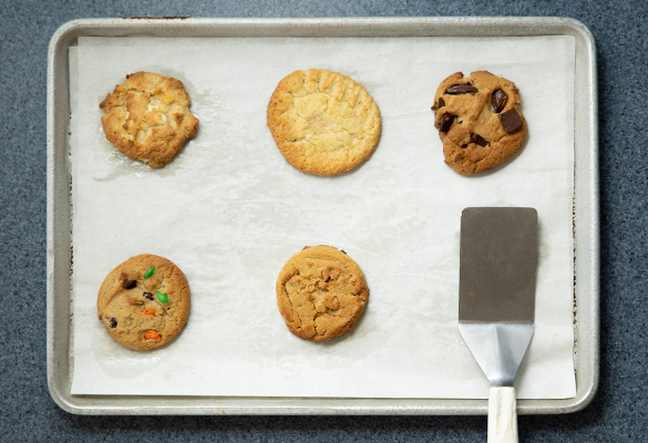 Photo of a variety of cookies on a sheet pan next to a spatula.