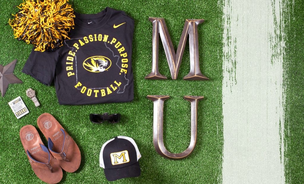 Products on a fake green grass background. Mizzou Nike t-shirt with state outline, Athletic tiger head and text "Pride. Passion. Purpose. Football."