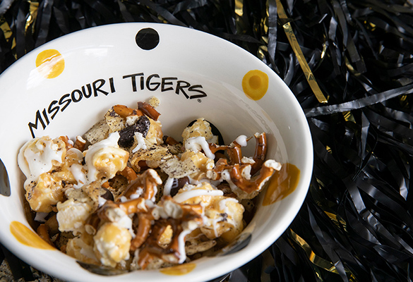 Photo of Mizzou Munch in a "Missouri Tigers" bowl next to a black and gold pom pom.