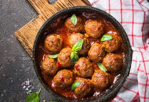 Photo of cranberry meatballs in a skillet with a checkered towel tucked at the side.