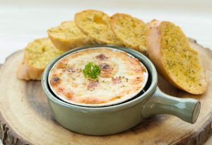 Photo of pizza dip in a green ceramic soup cup with garlic bread.