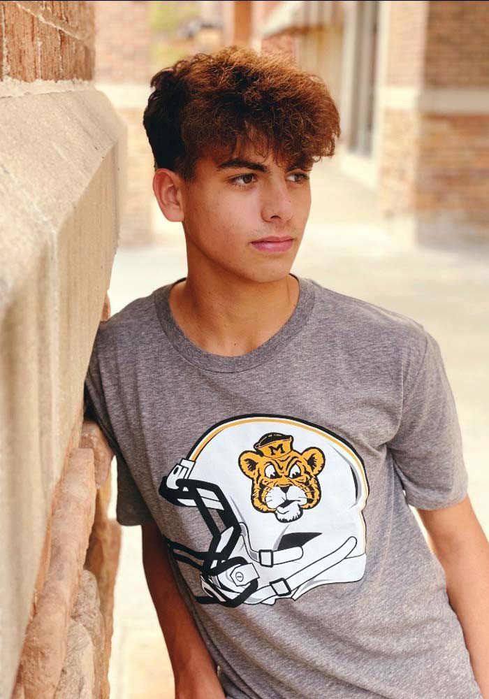 Man wearing gray shirt with graphic of helmet and vintage sailor tiger head mark.